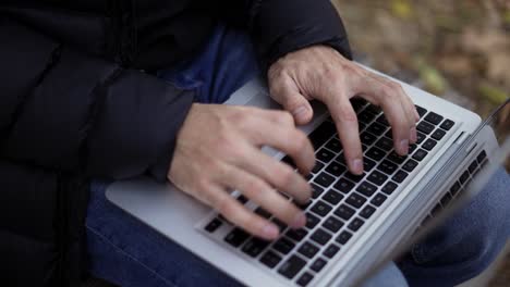 Unrecognizable-man-sitting-on-the-bench-in-the-park,-typing-on-the-laptop