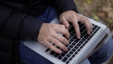 unrecognizable man sitting on the bench in the park, typing on the laptop