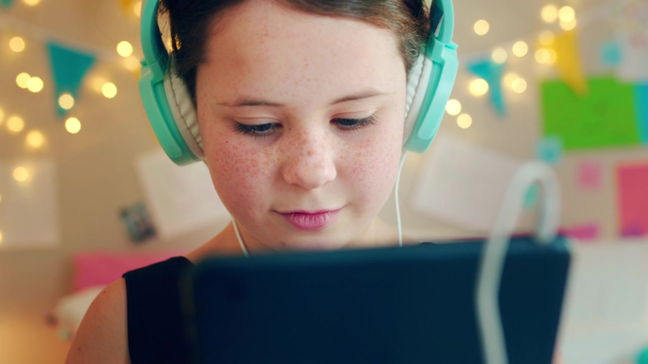 Ung pige med hovedtelefoner, der bruger en tablet på sit værelse