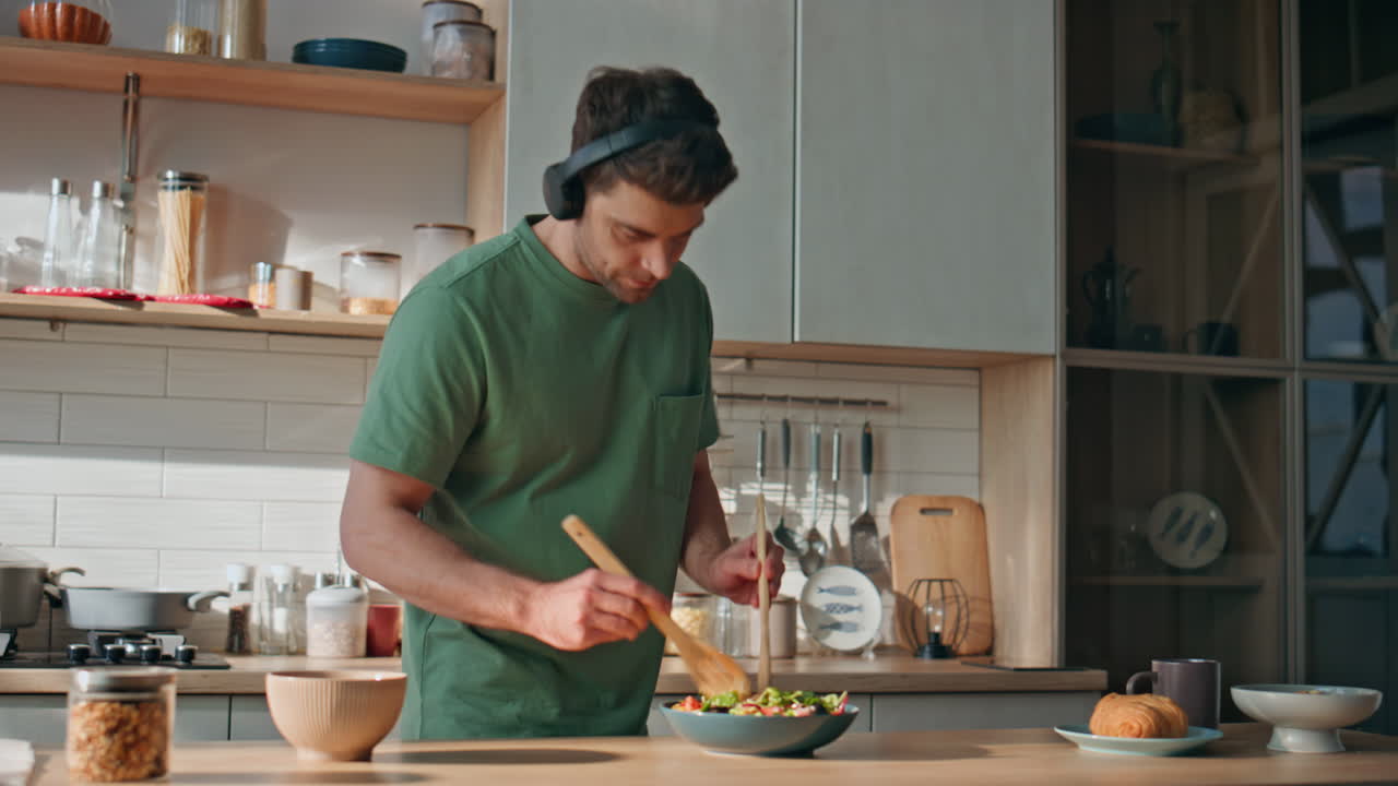 Guy earphones preparing food dancing along favorite song at kitchen closeup