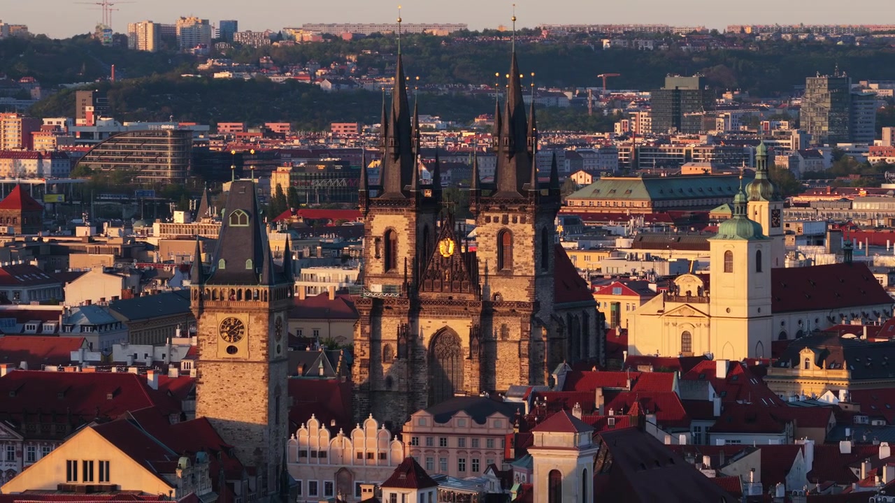 Veduta aerea con drone della Piazza della Città Vecchia con le torri gotiche gemelle della Chiesa di Tyn e la torre dell'orologio del Vecchio Municipio sopra i tetti rossi al tramonto.