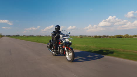 Motociclista-Monta-En-La-Carretera-En-El-Campo-Primavera-Campos-Verdes-Y-Cielo-Azul