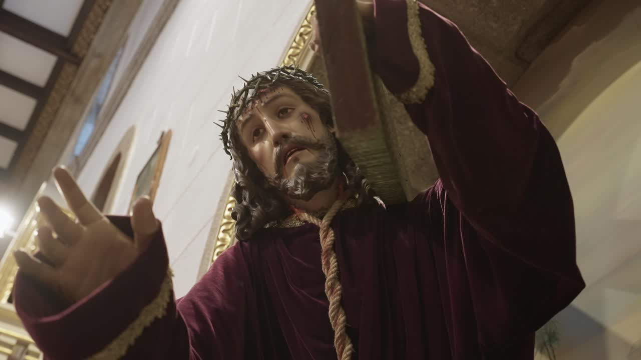 Primo piano di una statua di Gesù che sorregge una croce con la mano alzata all'interno di una chiesa