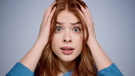 Ginger-woman-taking-head-in-hands-indoors.-Stressed-girl-posing-in-studio