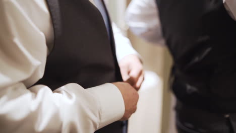 groom buttoning up his black suit vest in slow motion