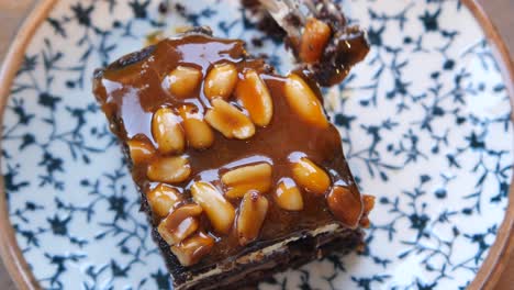 cerca de una rebanada de pastel de chocolate con salsa de caramelo y cacahuetes