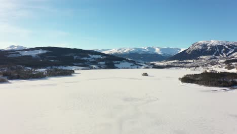 Reverse-aerial-over-frozen-massive-lake-Tunhovdfjorden-in-Norway-with-mountain-Dyna-and-Myking-in-background