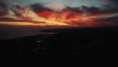 aerial of dramatic orange red sunset through the cloud with silhouette of coastline below