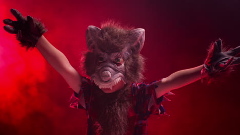 studio shot of child dressed up in werewolf monster costume trick or treating at halloween with red smoke background lighting scaring people