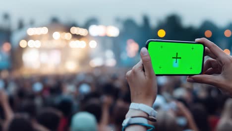 spectator recording live music concert with smartphone showing green screen