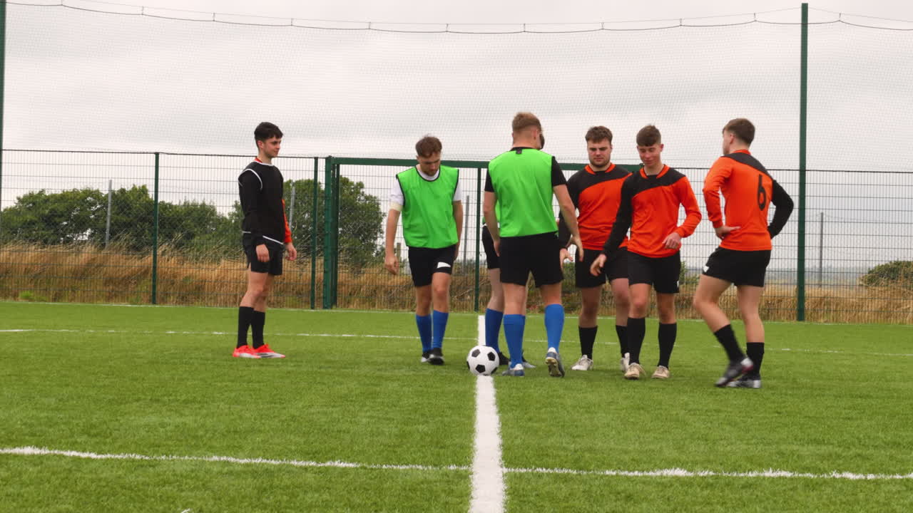 Soccer players preparing for kickoff on outdoor field, wearing green vests
