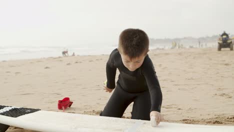 adorabile bambino che fa la ceretta con la tavola da surf sulla spiaggia