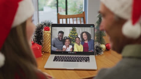 Rückansicht-Eines-Kaukasischen-Paares-Mit-Weihnachtsmützen,-Das-Während-Der-Weihnachtszeit-Einen-Videoanruf-Auf-Dem-Laptop-Führt