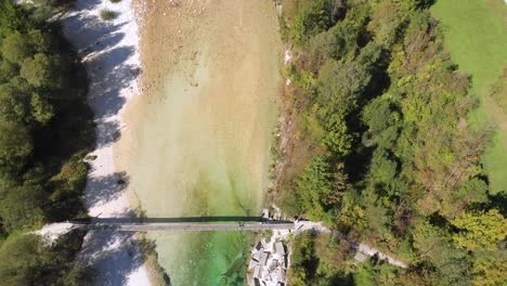 aerial top down view of rope bridge over beautiful emerald river, man walking across