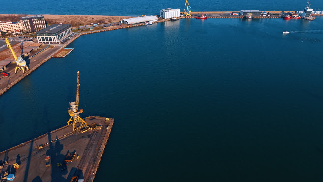 Вид с воздуха на коммерческий морской порт с желтыми кранами. Портовая инфраструктура, желтые грузовые краны, синяя вода и промышленные здания на закате.