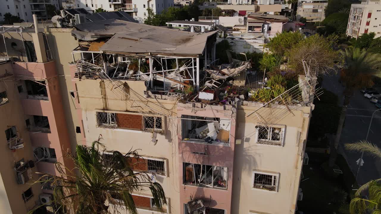 Circular drone view of a Tel Aviv building hit by an Iranian missile. Roof and apartments are destroyed. Surrounding buildings appear intact.