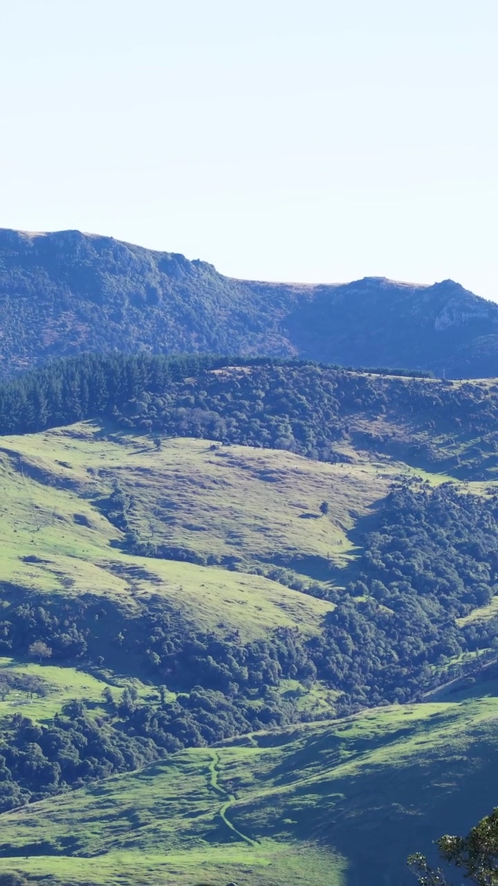 Un paesaggio sereno di colline verdi lussureggianti e montagne distanti sotto un cielo limpido, catturato con un delicato movimento della telecamera.