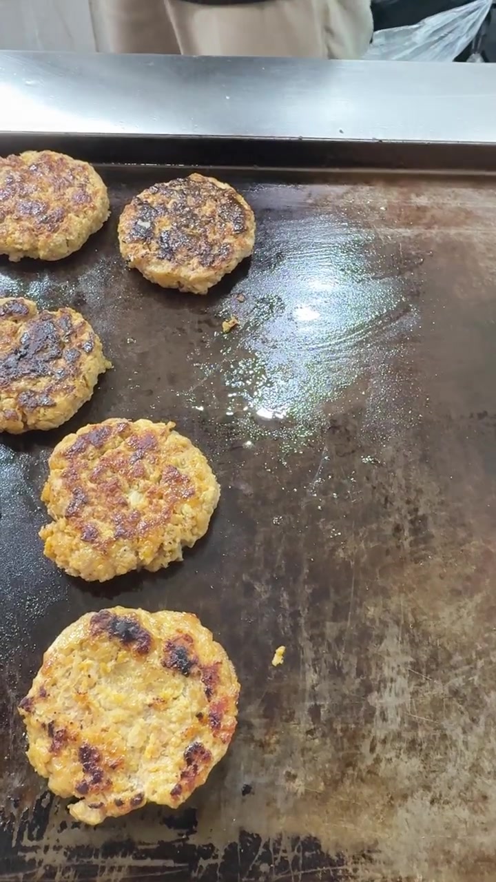 Chef Using Tongs to Flip Burger Patties on a Hot Griddle