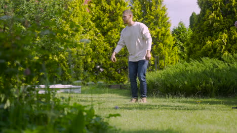 Side-view-of-caucasian-young-man-playing-petanque-in-the-park-on-a-sunny-day