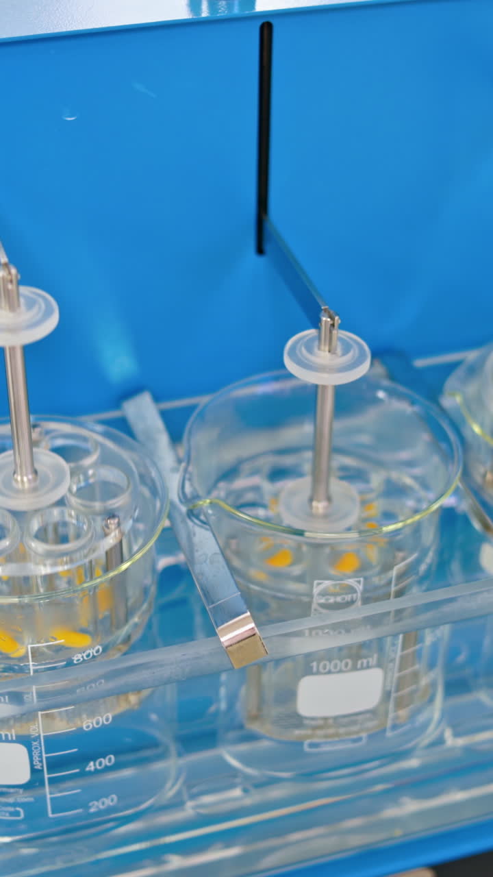 Experiments at the lab. Sliding shot of a dissolution apparatus testing medication pills dissolving tablets in liquid. Laboratory routine. Vertical video