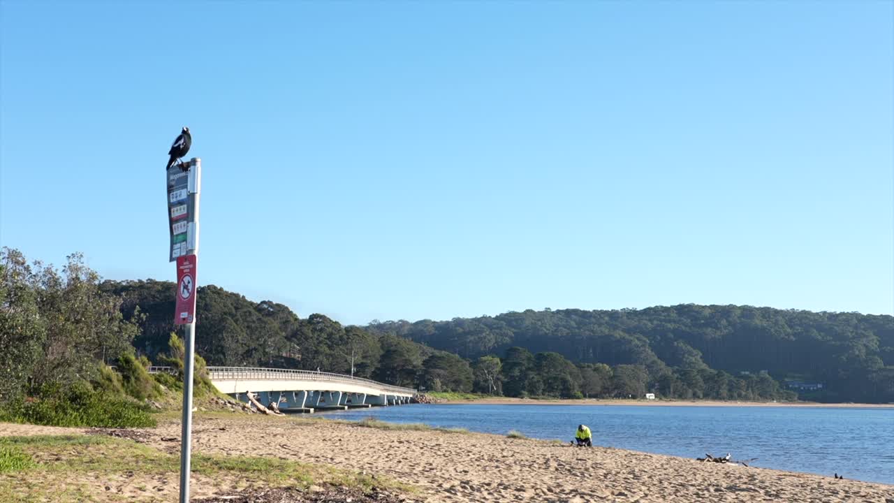 Spiaggia sabbiosa con ponte costiero e cartello segnaletico in primo piano, Tathra, Nuovo Galles del Sud, Australia