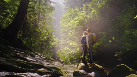 a pair of travelers are photographed in a picturesque place in a forest near a mountain river 4k vid