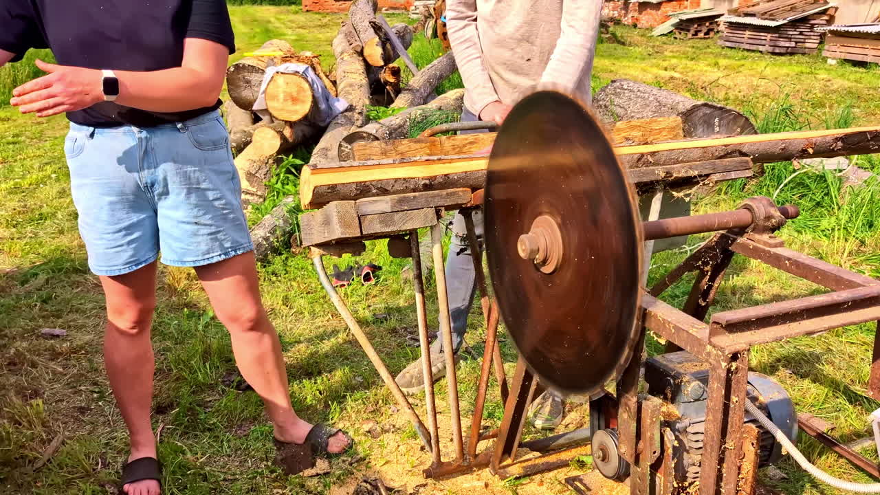 Farming family cutting log wood with rusty vintage mechanical circular saw outdoors for firewood
