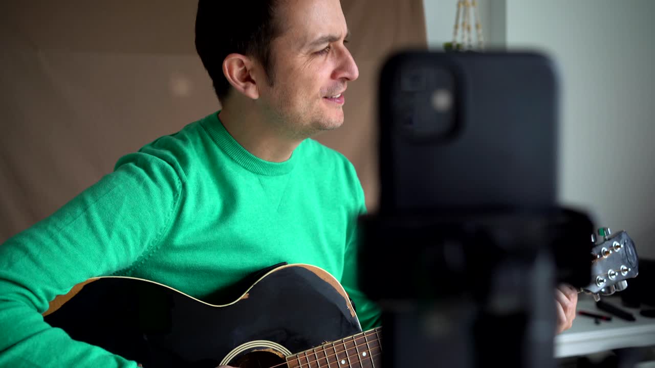 músico sonriente con video de grabación de guitarra en el teléfono inteligente