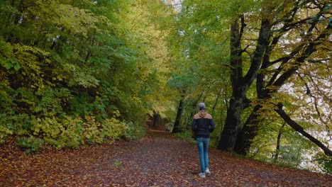 Un-Joven-Alto-Con-Gorra-Camina-Con-Las-Manos-En-Los-Bolsillos-Por-Un-Camino-Hacia-El-Bosque-De-Gyllebo-En-Otoño,-Al-Sur-De-Suecia-Österlen---Tiro-Ancho-Estático