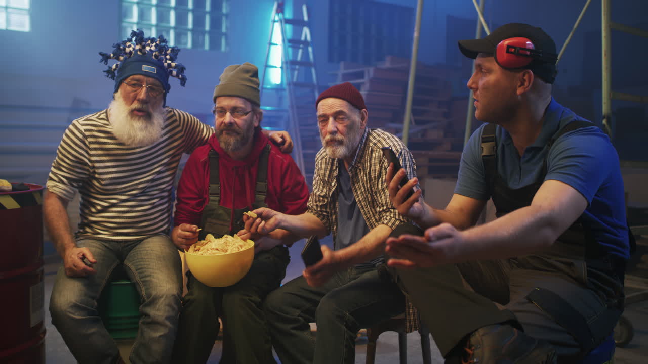 Four men taking a break in a workshop, eating snacks and looking at phones