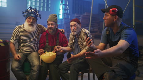 four men taking a break in a workshop, eating snacks and looking at phones
