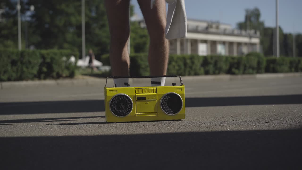 Vintage tape recorder on asphalt road with unrecognizable young Caucasian sportsman approaching, turning off musical device, and leaving. Retro style sport concept.