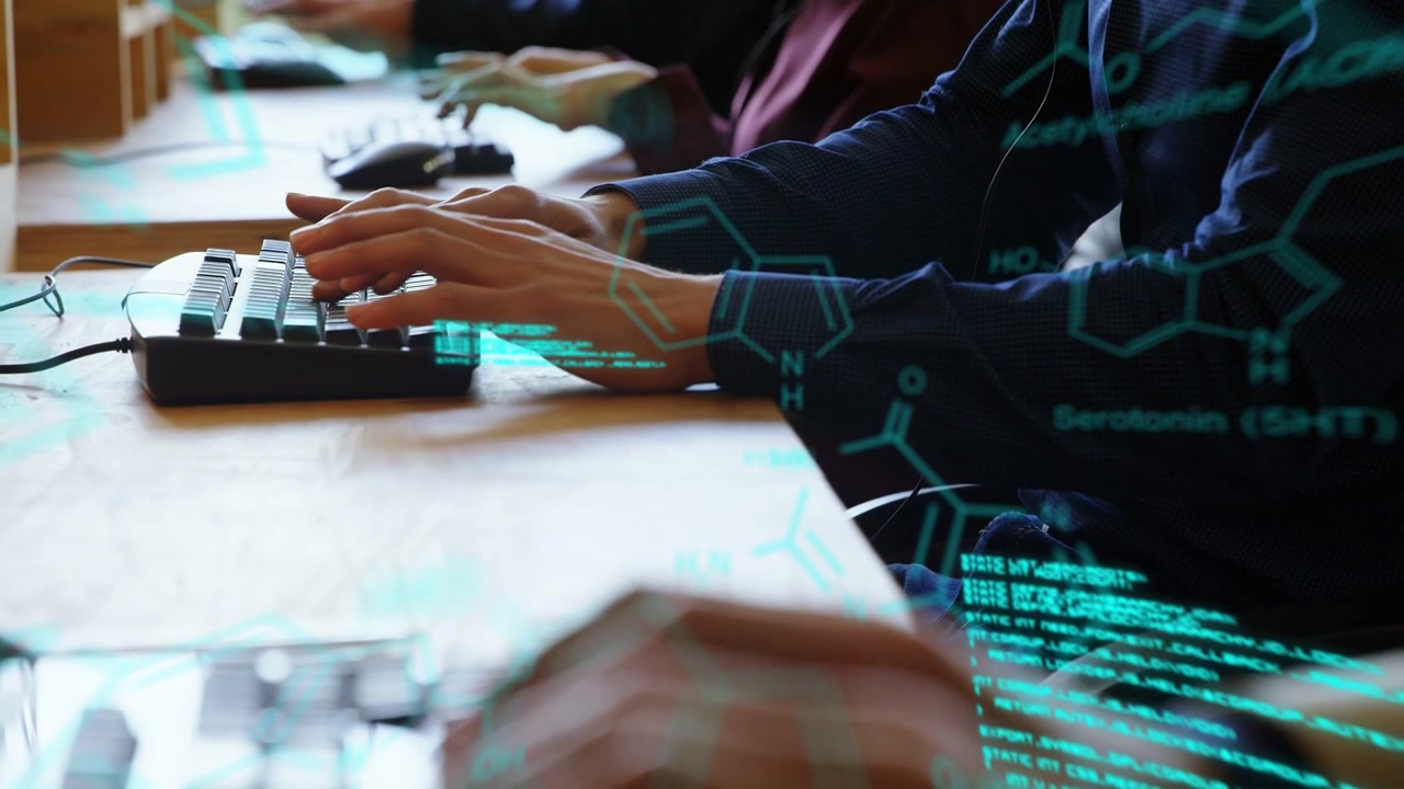 Typist's hands typing at shared desk, activating scrolling teal code and molecule graphics for tech