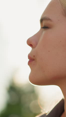 mujer sentada al aire libre bebiendo jugo de naranja con una expresión refrescante, disfrutando de un momento de relajación, el fondo presenta luz suave y brillante y vegetación