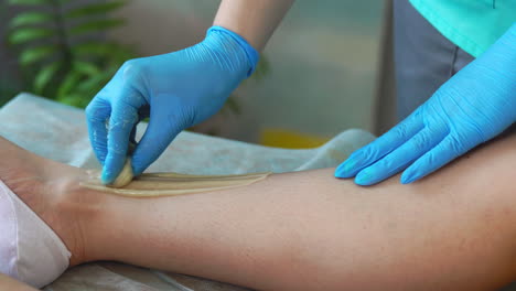 gros plan dans le salon de beauté maître en gants faisant la procédure pour enlever les poils sur les jambes avec un mélange de sucre