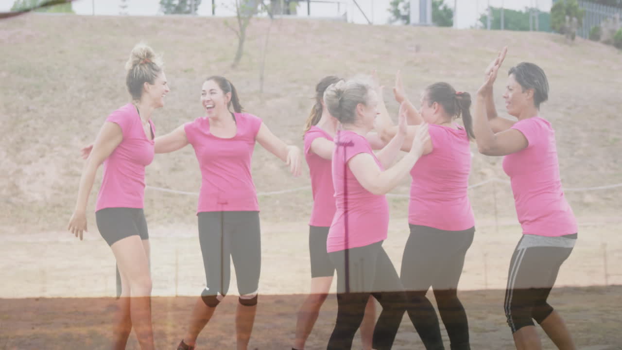 Celebrating outdoors, women in pink shirts high-fiving with joy and animation