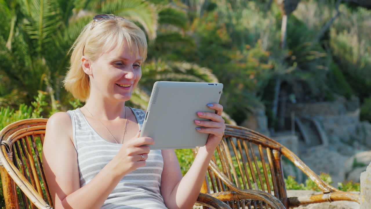 женщина турист с планшетом говорит, что сидит в плетеном кресле на фоне пальм всегда