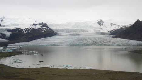 Iceland-glacier-with-water,-green-grass,-blue-ice-and-fog-with-drone-video-moving-up