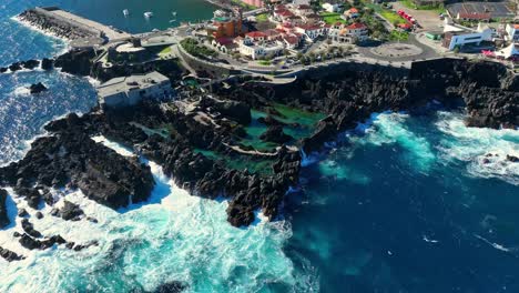 ocean waves crash against jagged rocky basalt in porto moniz natural pools, aerial