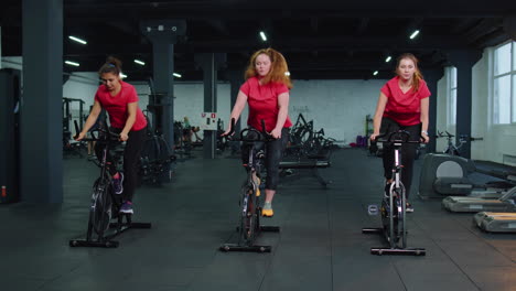 Healthy-Caucasian-group-of-women-exercising-workout-on-stationary-cycling-machine-bike-in-gym