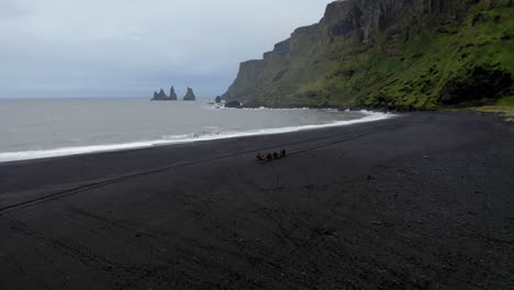 aerial: slow orbit shot with group of tourists riding horses on the beach of vik in iceland