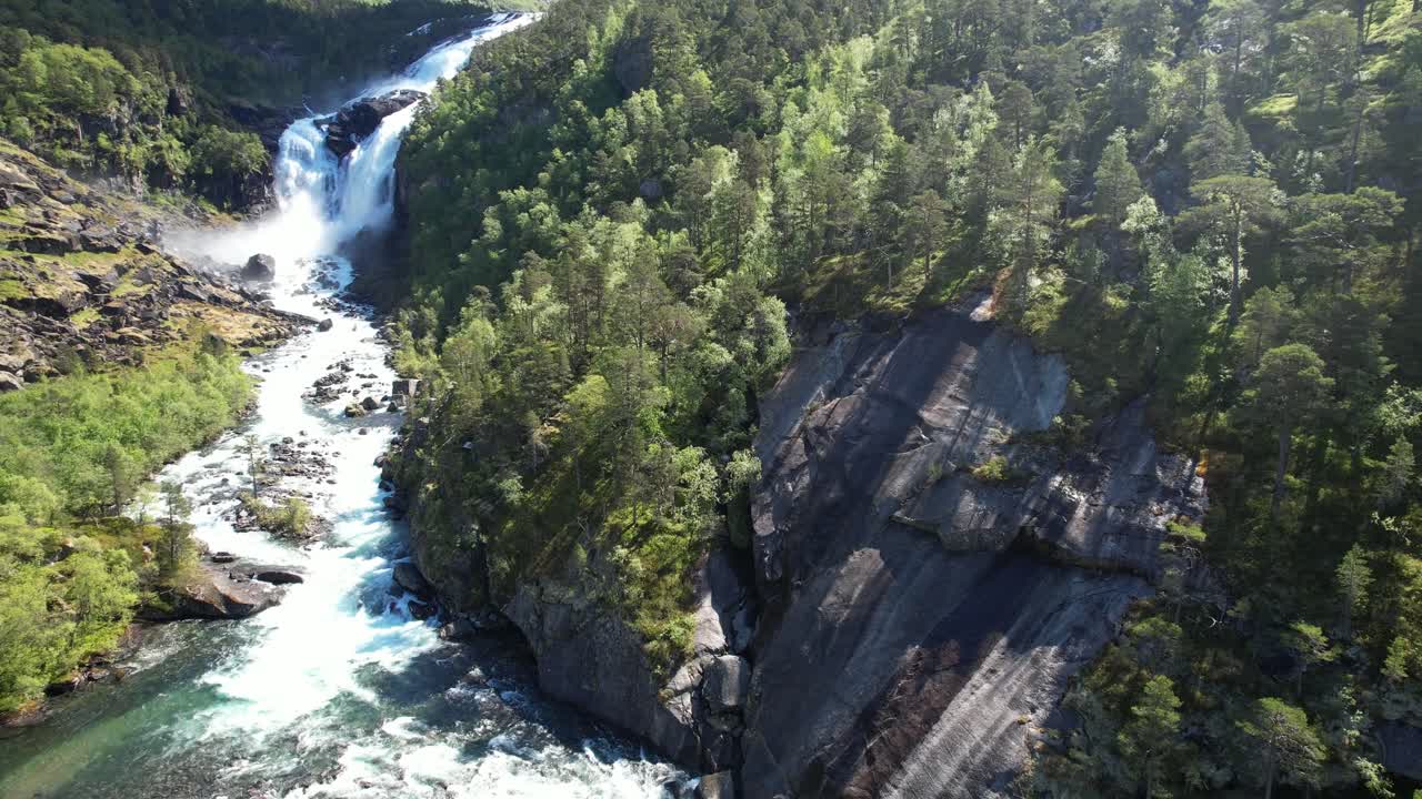 Una ripresa aerea scende dall'alto di una cascata fino al fiume Kinso e alla valle boscosa vicino a Hardangervidda, in Norvegia.