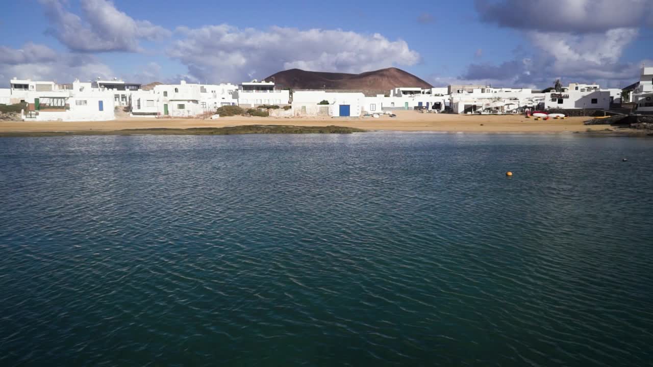 video de una costa en la graciosa en españa donde sopla el viento y hay edificios y casas blancas mientras el horizonte es visible en la distancia tomada durante un día soleado con nubes