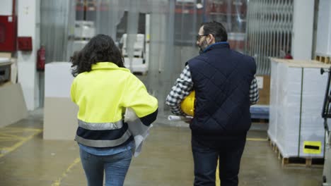 back view of two factory workers walking with blueprints