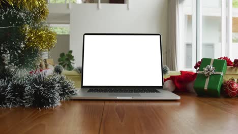 Laptop-with-copy-space-on-screen-on-table-with-santa-hats,-decorated-christmas-tree-and-presents