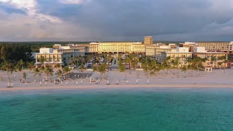 Man,-unrecognizable,-running-on-sand-beach-with-palm-trees-at-sunset,-luxury-vacation-resort-in-the-background,-romantic-lifestyle-in-the-Caribbean,-Punta-Cana,-Dominican-Republic