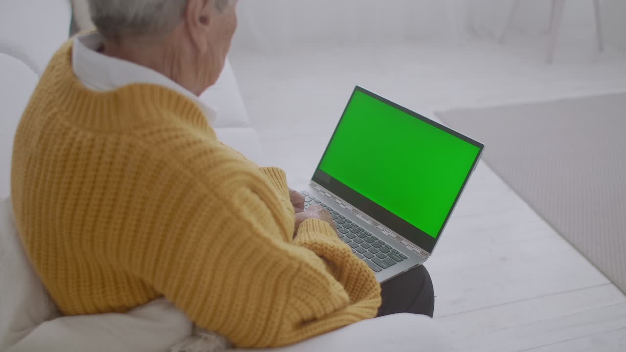 mujer madura asintiendo con la cabeza sí mientras mira una computadora de pantalla verde. mujer madura anciana con cabello gris y una videollamada en su computadora portátil. computadora portátil con pantalla verde