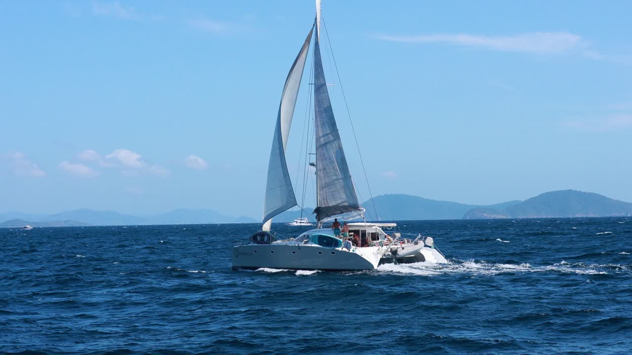 A sailboat glides across the ocean near Ko Racha Yai, Phuket, under clear blue skies and bright sunlight