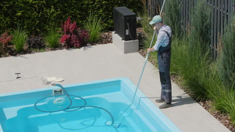 worker in overalls vacuuming the pool in the backyard of the house. top view