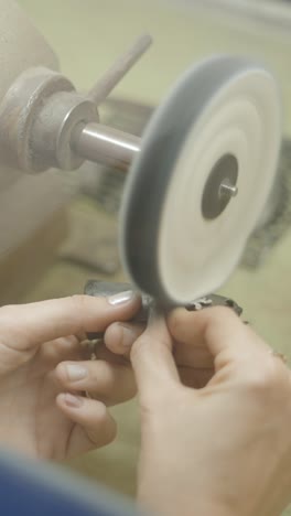 hands polishing metal on a grinding wheel in a workshop